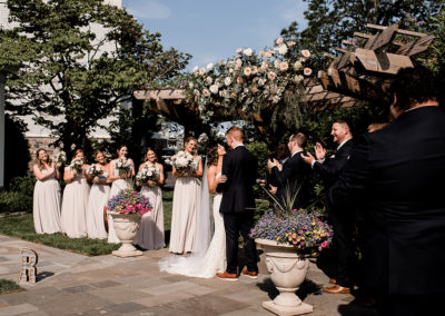 Outdoor wedding ceremony of bride and groom at the altar with officiant and bridal party beside them at the Ceremony Garden.