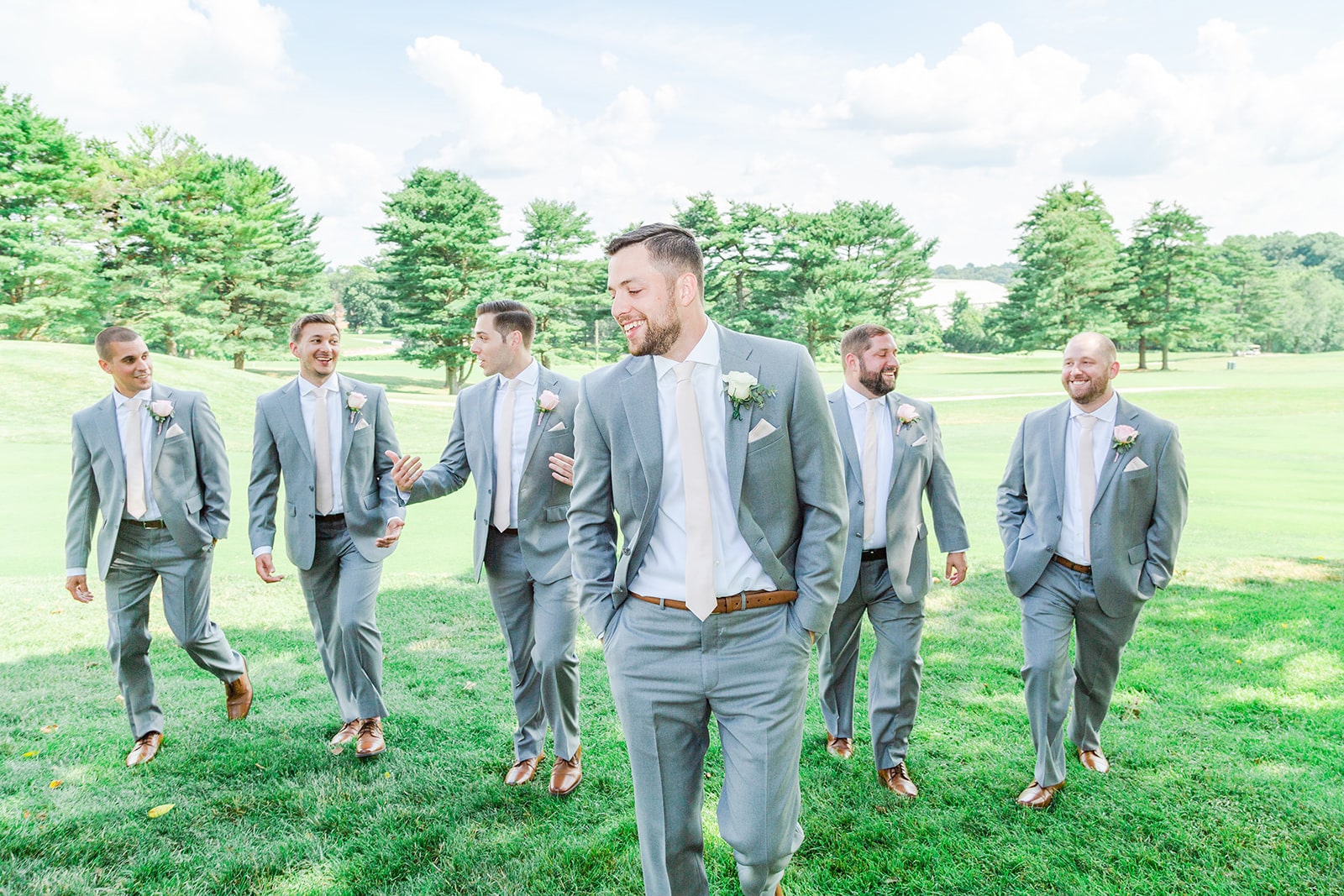 Groomsmen walking together in a golf course fairway towards the wedding. Photo by Chesapeake Charm Photography