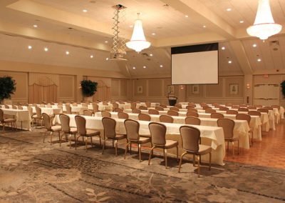 Corporate event set up with single projector with tables in front of each row of chairs.