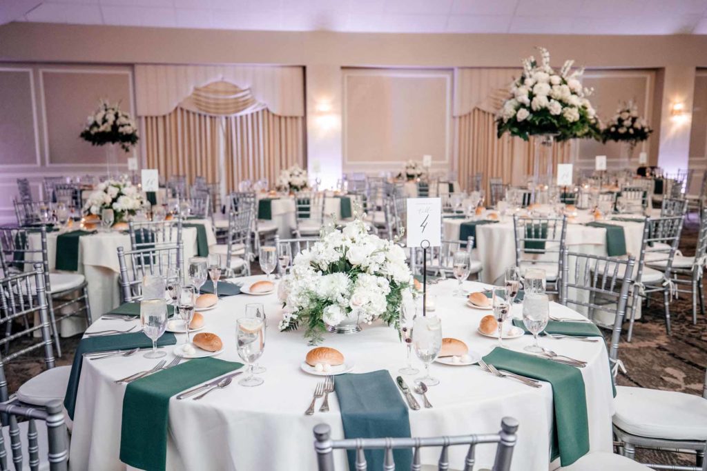 Wedding dinner setup with white table cloths and emerald napkins. Photographed by: Duca Studio