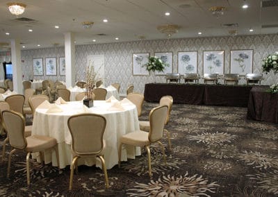 Fairway Ballroom with white round tables with pussy willow centerpieces surrounded by tan and gold chairs. Floral patterned walls and carpets with buffet table with chafing dishes.