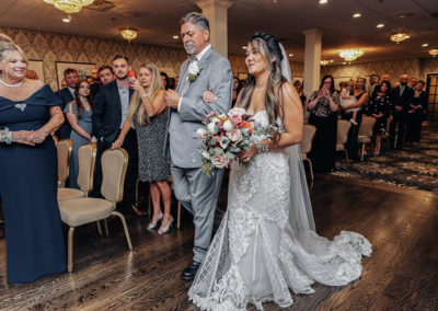Indoor wedding ceremony in the Fairway Ballroom. Bride and father are walking down the aisle as guests watch.