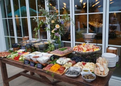 Cold display of appetizers on wooden table in front of glass wall.