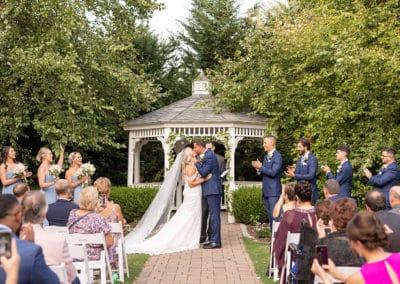Outdoor wedding ceremony at the Gazebo. Bride and groom kissing at altar and bridal party cheering.