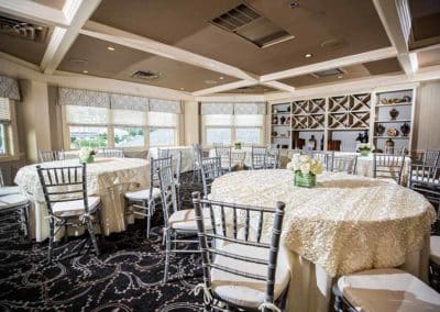 Reserve Room at Springfield Country Club decorated in off white and with silver chairs around round tables with flower center pieces.