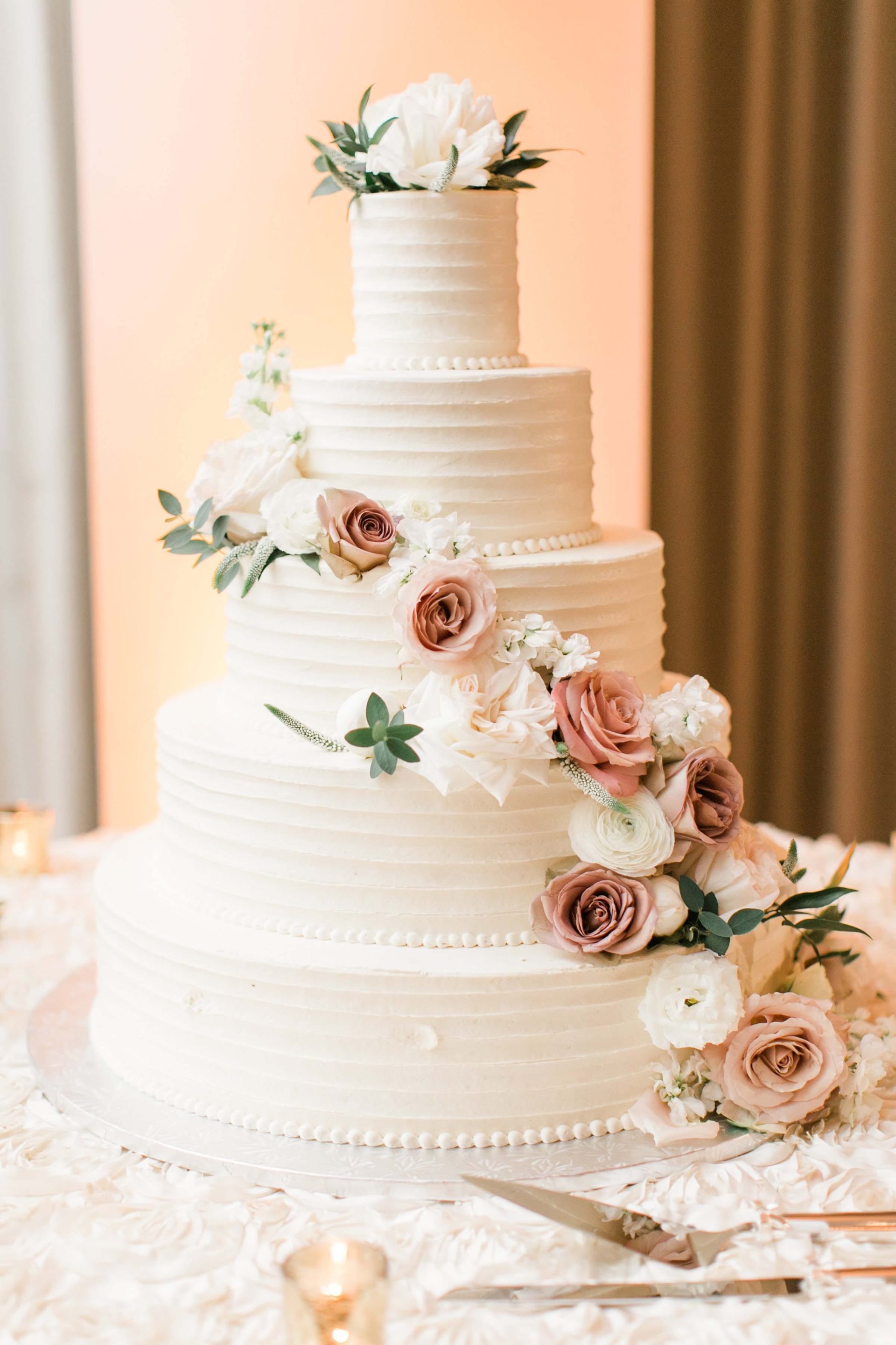Five layer wedding cake with white icing and garland of fresh flowers.