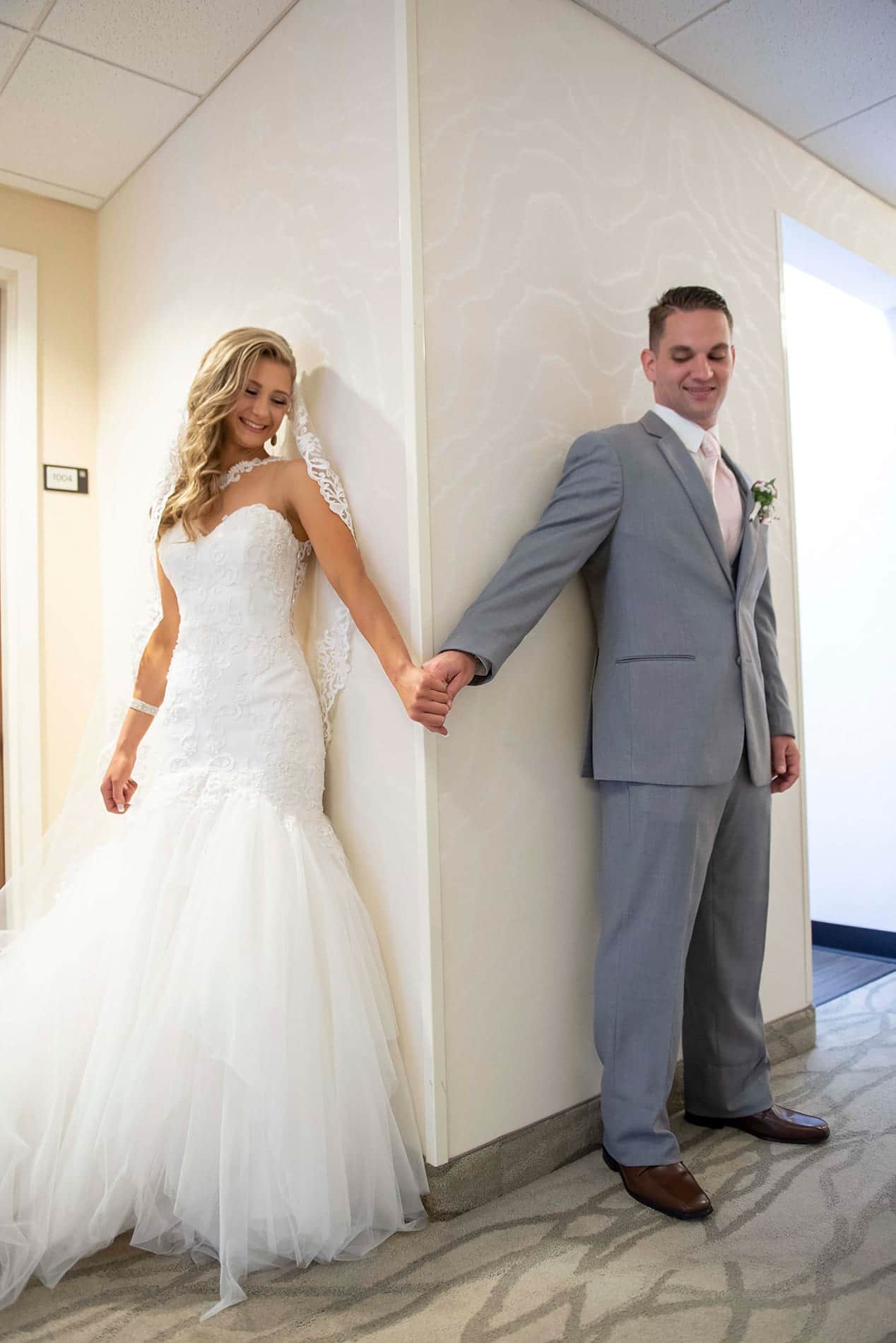 Bride and Groom holding hands around a corner before they can see each other.Part of first look wedding ideas blog.
