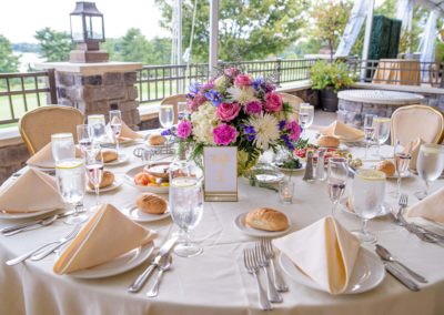 Table setting with white linen, pink and purple floral centerpiece with golf course in the background.